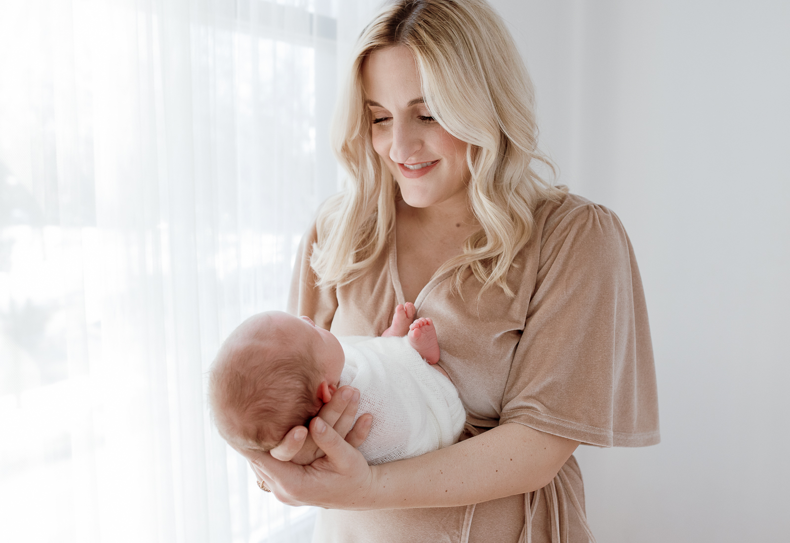 Wearing a velvet flutter sleeve dress, Detroit, Michigan's Laurel Smith Photography captures this new mom cradling her newborn baby. white translucent curtain, white studio plymouth michigan newborn photos, professional plymouth michigan newborn photographer, laurel smith photography, womens tan velvet flutter sleeve dress, newborn in white muslin swaddle #DetroitMichiganFamilyPhotographer #DetroitMichiganPhotographer #FamilyPhotoOutfitInspiration #PlymouthMichiganFamilyPhotographer #PlymouthMichiganPhotographer #ExtendedFamilyPhotos #DetroitMichiganFallFamilyPhotos #LetThemBeLittle #LetTheKids #DetroitMichiganLifestylePhotographer