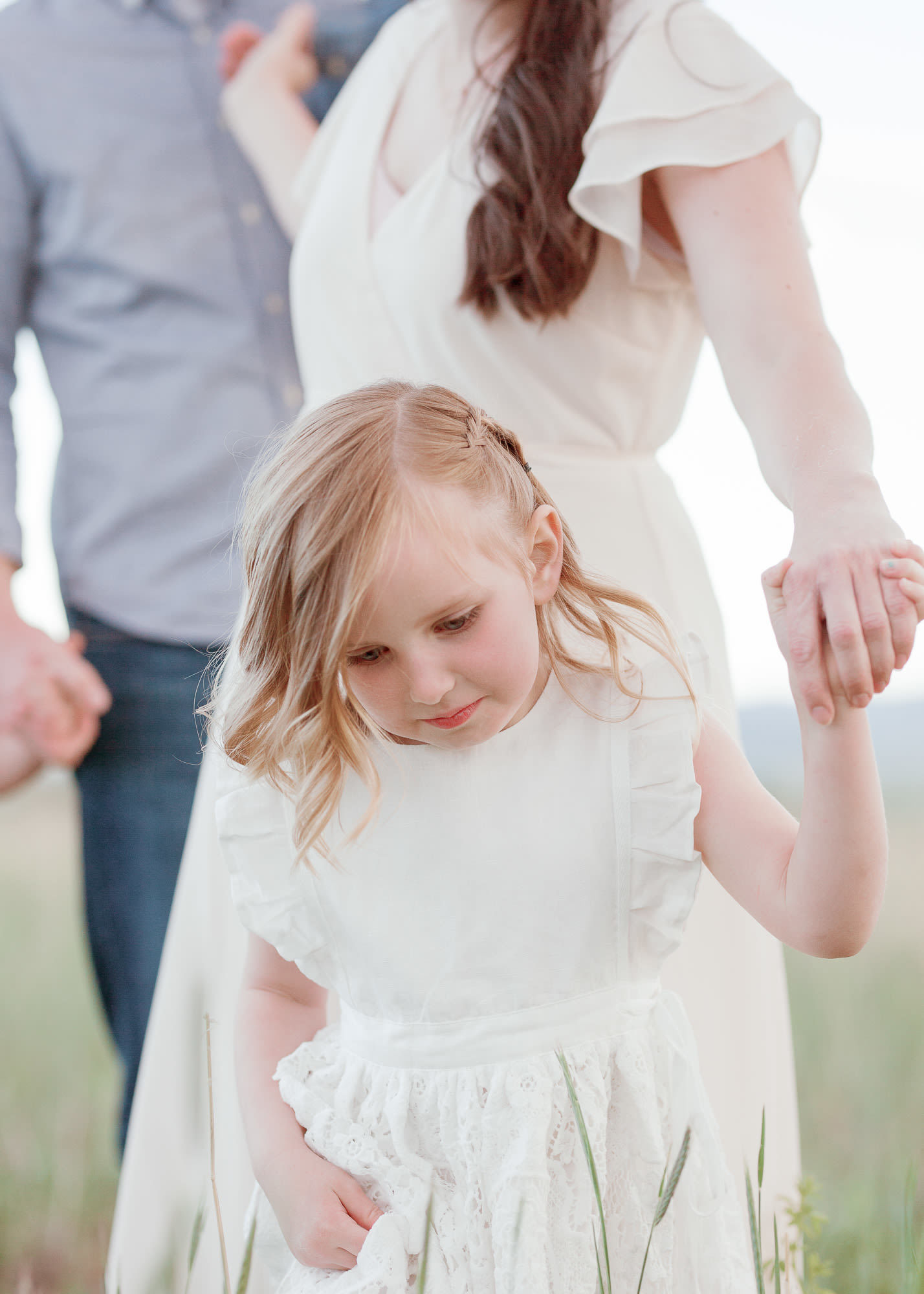 little girl holding her parents' hands in a field