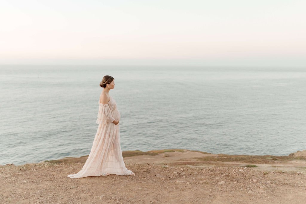 woman standing on beach with ocean in the background during her maternity photo session in san francisco