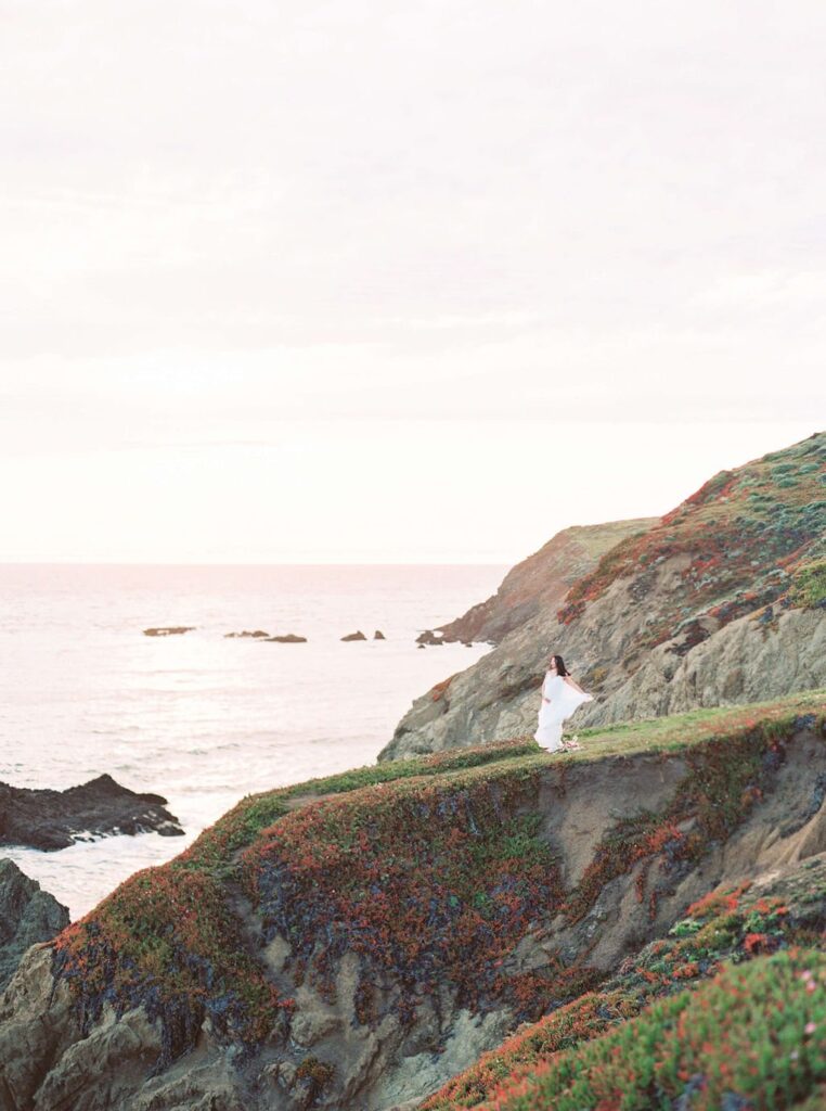 wide shot of woman on cliff with ocean in the background during her maternity photos in san francisco