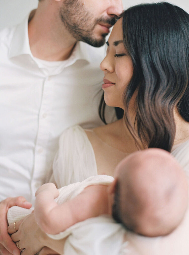 Newborn photo studio San Francisco designed for calm, comfortable newborn sessions. Mama holds baby while dad rests his face on Mama's forehead. 