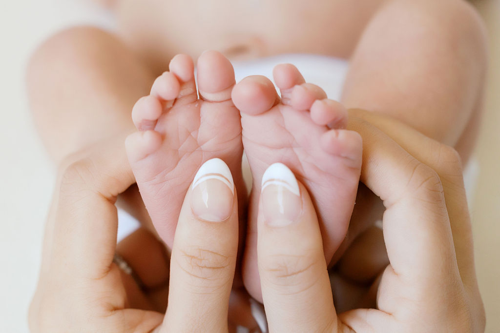 Close-up of a newborn baby’s tiny feet gently held between a parent’s fingers, highlighting soft skin and delicate details in a light-filled newborn photography session