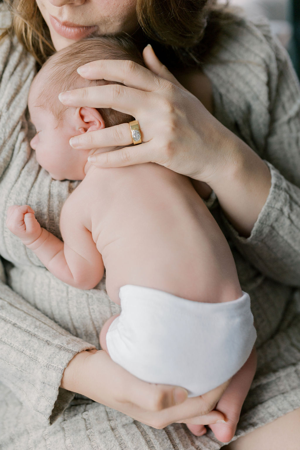 Newborn baby resting against a mother’s shoulder wearing a simple white diaper, with the mother’s hand gently cupping the baby’s head and a soft kiss pressed to the crown, highlighting connection and care in a moment often captured by bay area newborn photographers