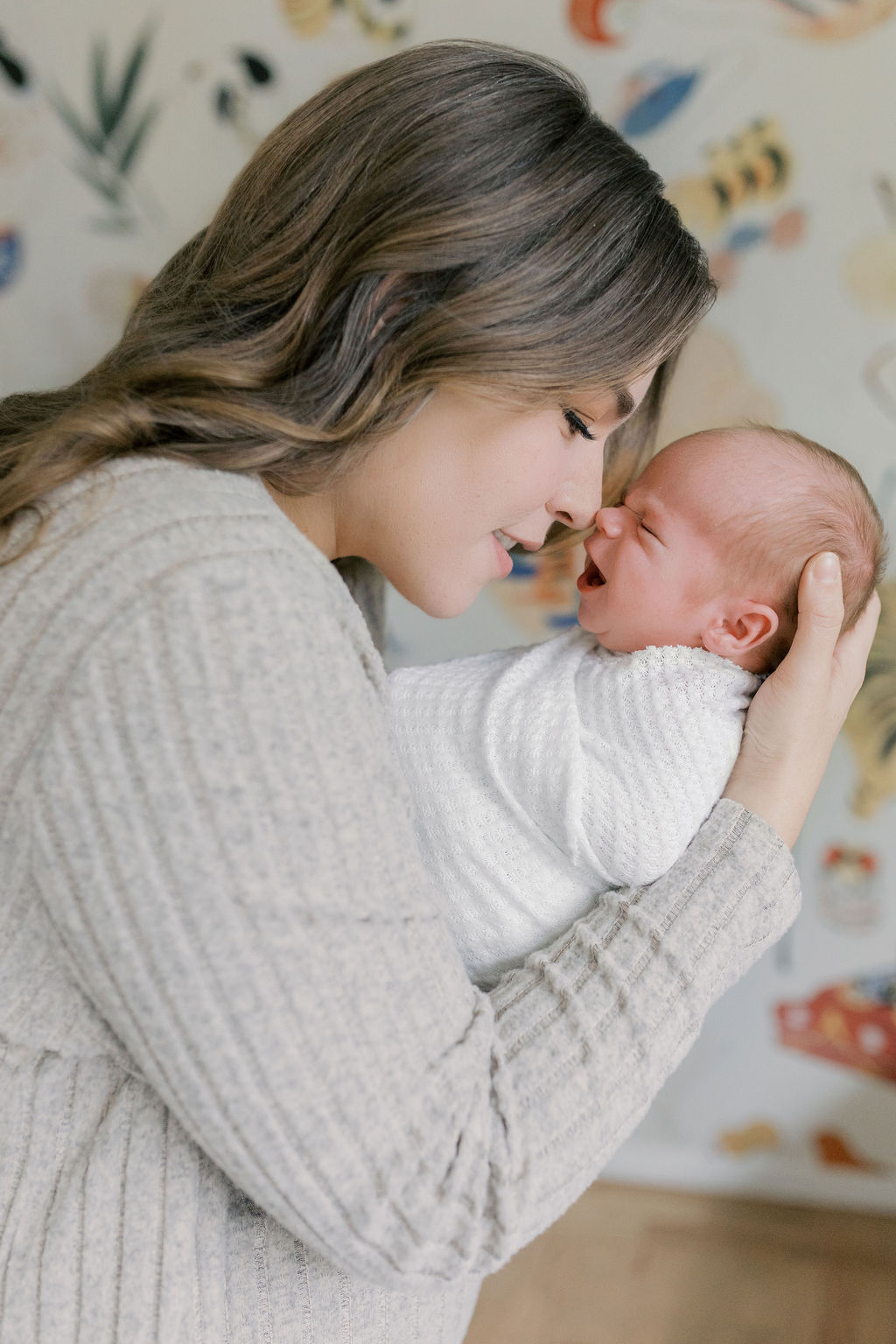 Mother holding her swaddled newborn close and leaning in nose-to-nose as the baby’s mouth opens in a small expression, soft patterned wall in the background and gentle light emphasizing their connection, a heartfelt moment captured by a bay area professional newborn photographer