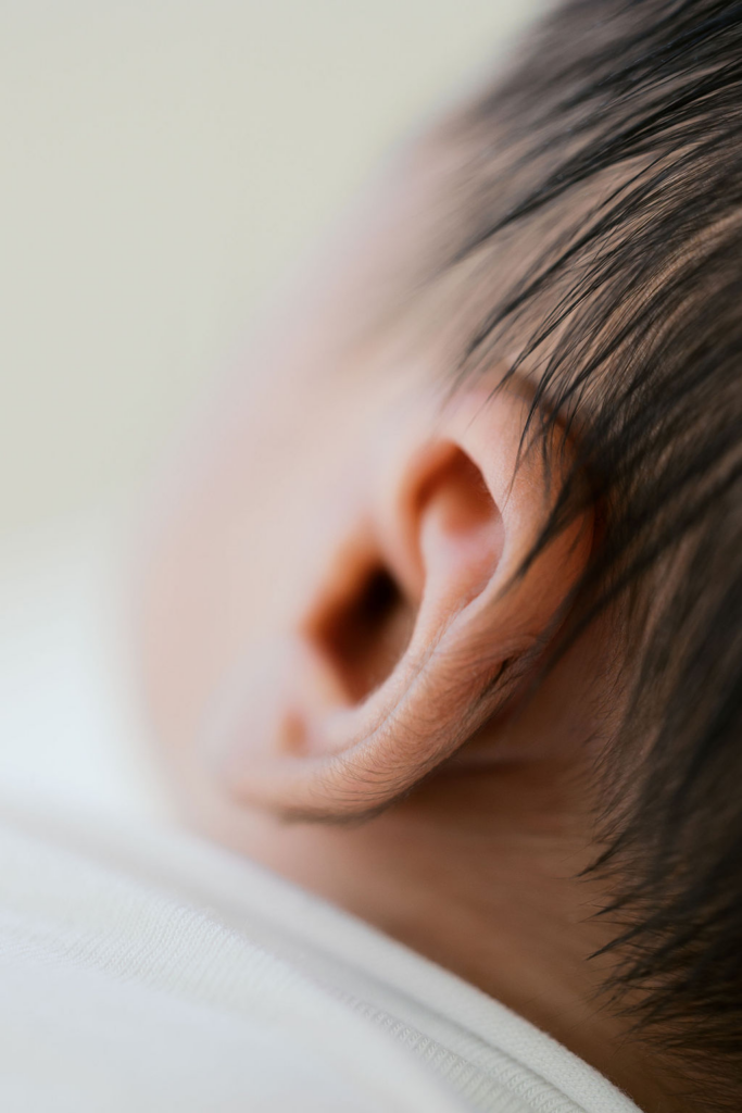 Macro detail of a newborn baby’s ear and fine dark hair, with soft skin texture and gentle curves of the ear highlighted against a creamy blurred background, illustrating the kind of detail to notice when learning how to choose a newborn photographer