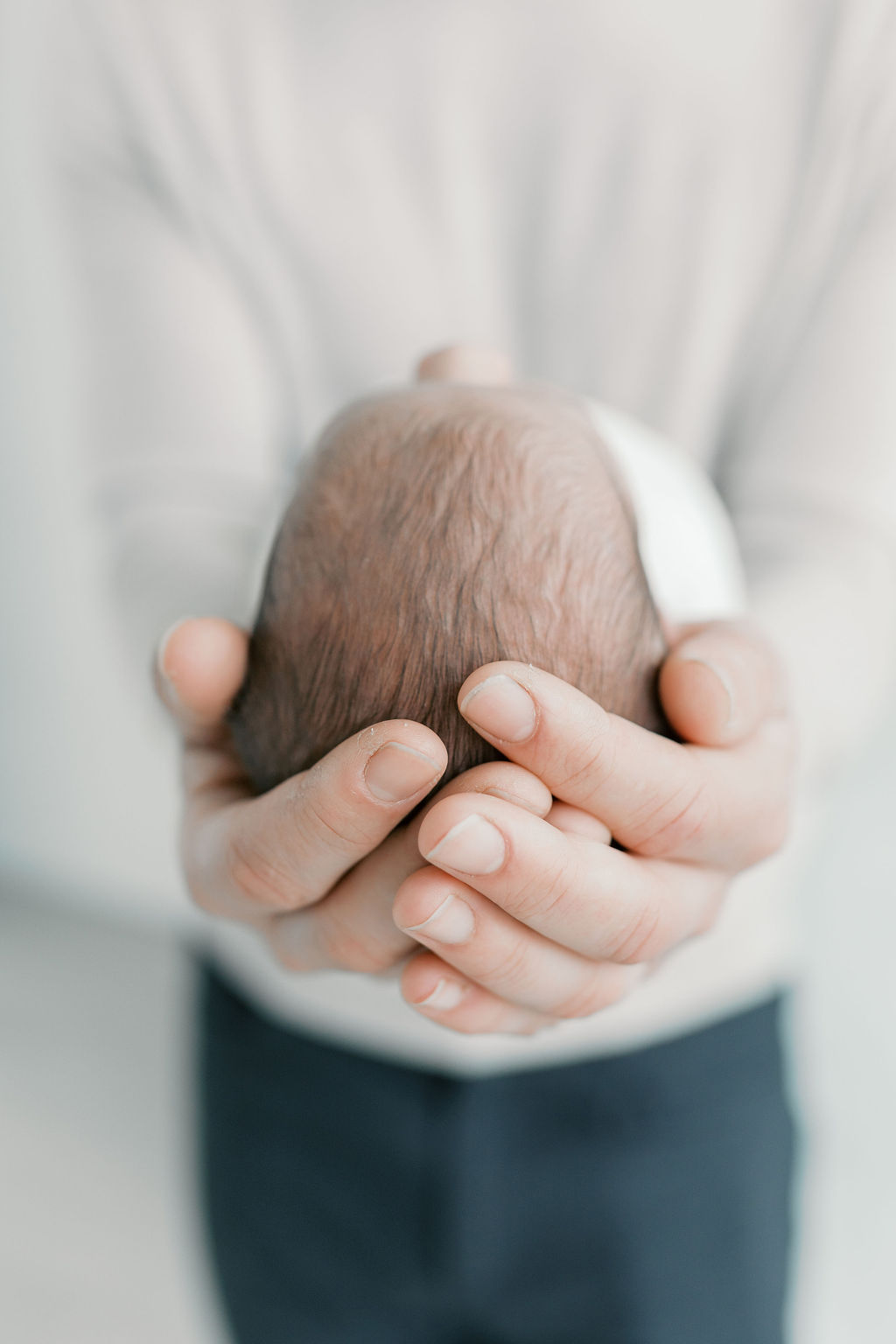 Close-up of a parent’s hands gently cradling the back of a newborn’s head, highlighting fine hair texture and the small scale of the baby against adult hands in a tender moment captured by a bay area professional newborn photographer