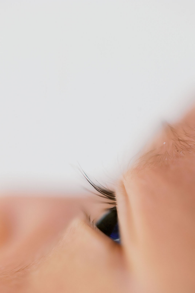 Extreme close-up of a newborn baby’s partially open eye with long delicate eyelashes and soft peach-toned skin, captured in bright diffused light with shallow depth of field by the best newborn photographer bay area