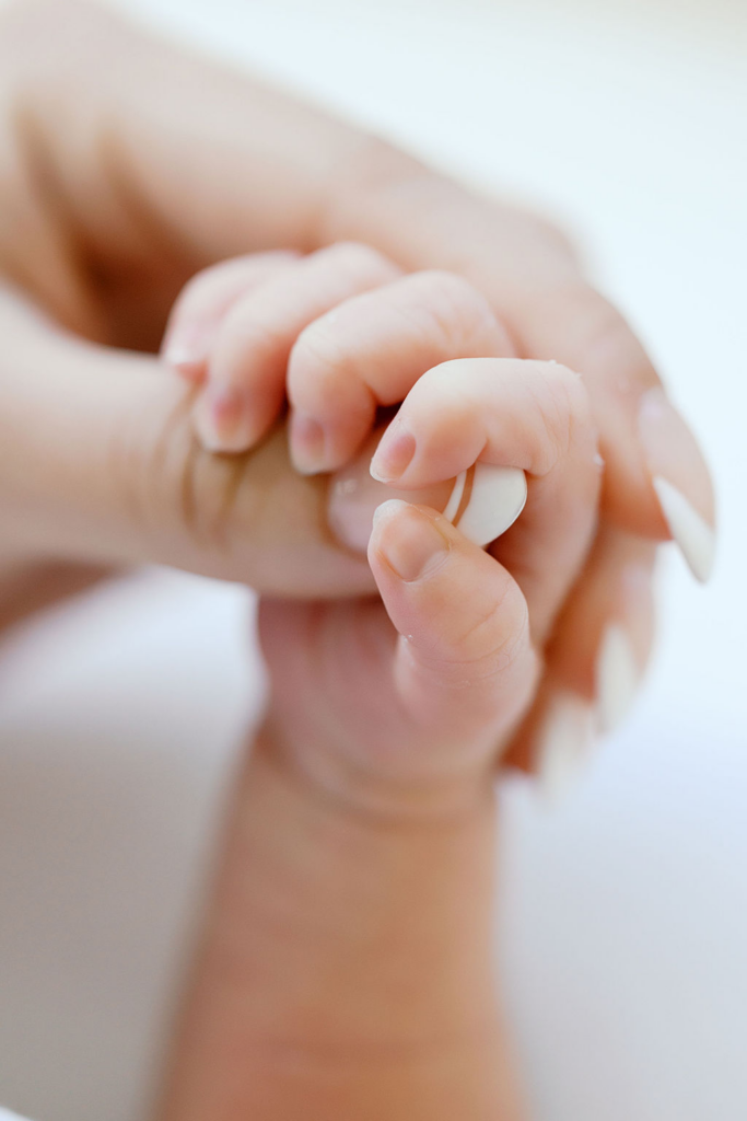 Close-up of a newborn baby’s tiny hand gripping an adult’s finger, showing delicate fingernails, soft skin folds, and a gentle connection between parent and child, a moment often highlighted by bay area newborn photographers