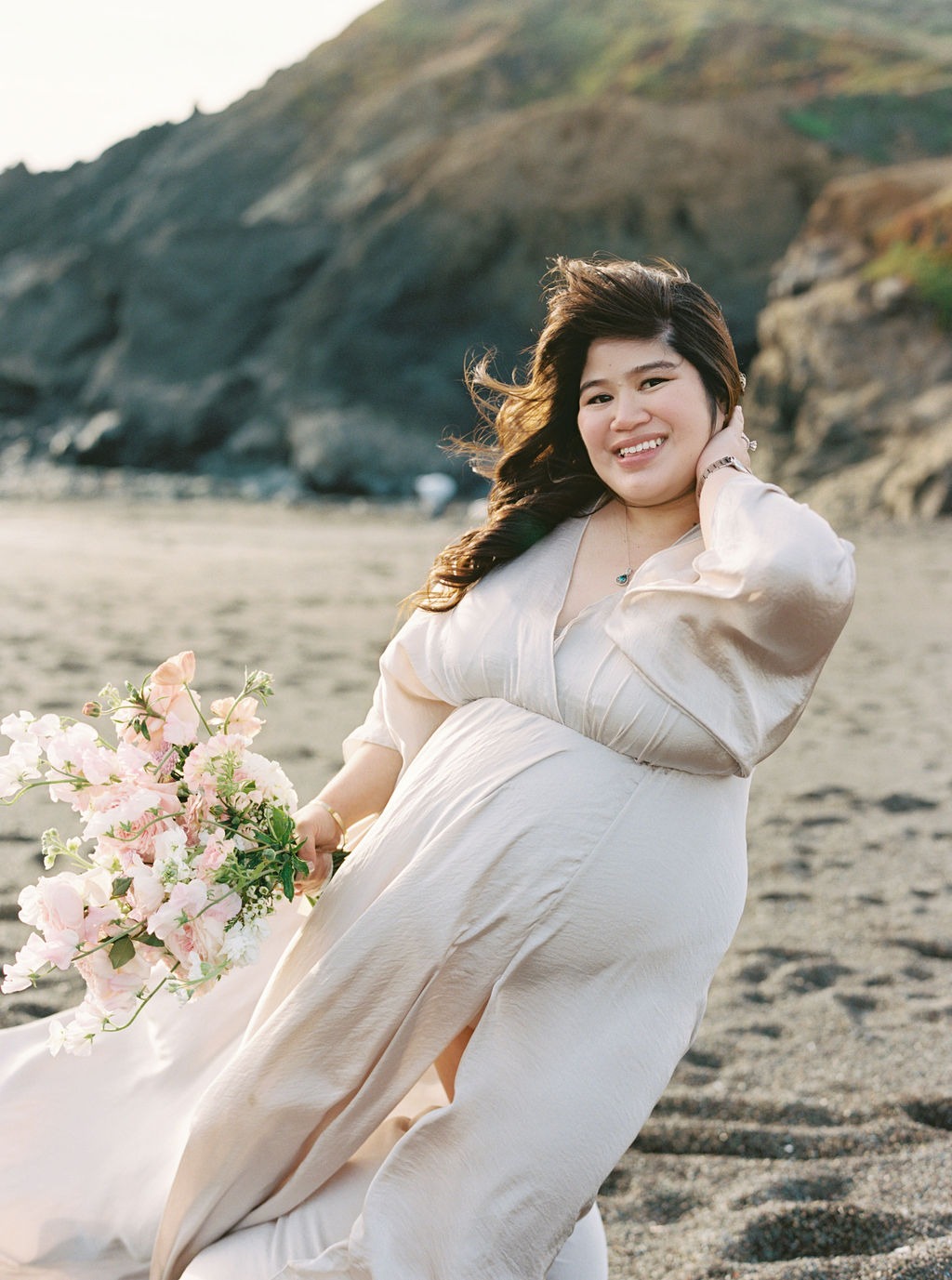 woman in a flowy champagne colored dress holding a rose gold toned bouquet on rodeo beach ca