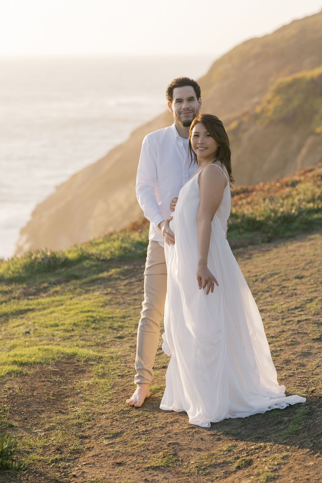 couple smiling at the camera during their maternity photoshoot at rodeo beach ca