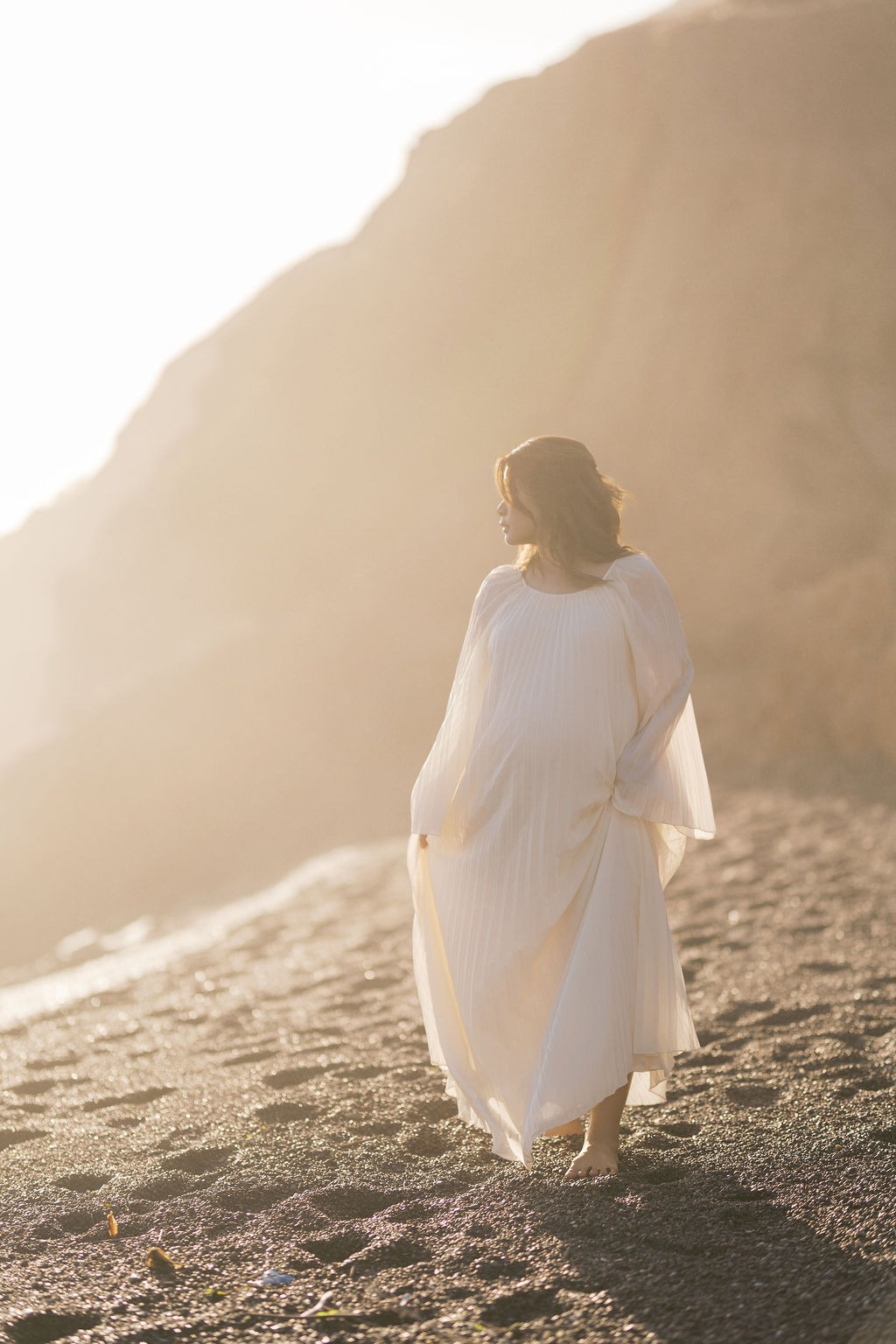 woman slowly walking on rodeo beach ca during her maternity photoshoot