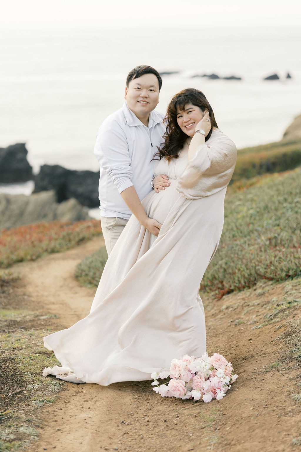 man placing his hand beneath a woman's pregnant belly while smiling during their rodeo beach san francisco ca maternity photoshoot