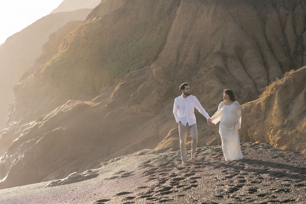 couple walking along the rodeo beach ca while holding hands during their maternity photo shoot