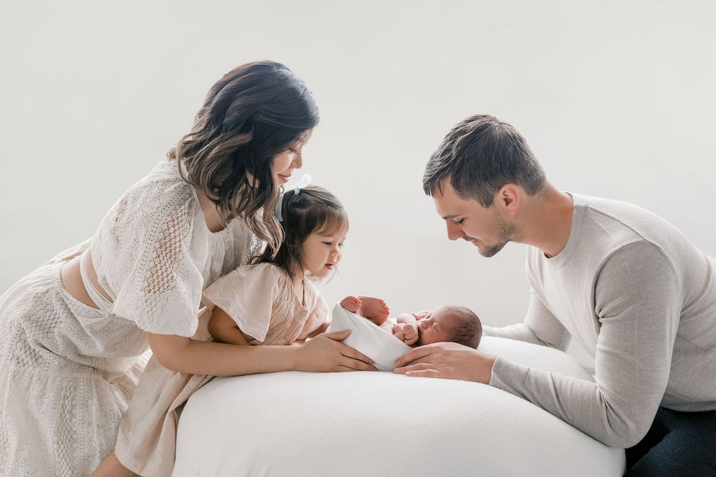 mother, father, and sister holding and staring at newborn during their newborn family photo session