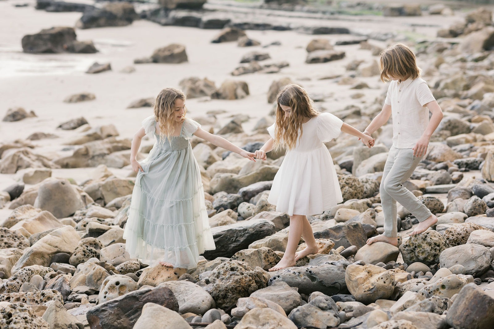 photograph of three siblings walking on a rocky beach during their family photoshoot at one of the best san francisco photo shoot locations