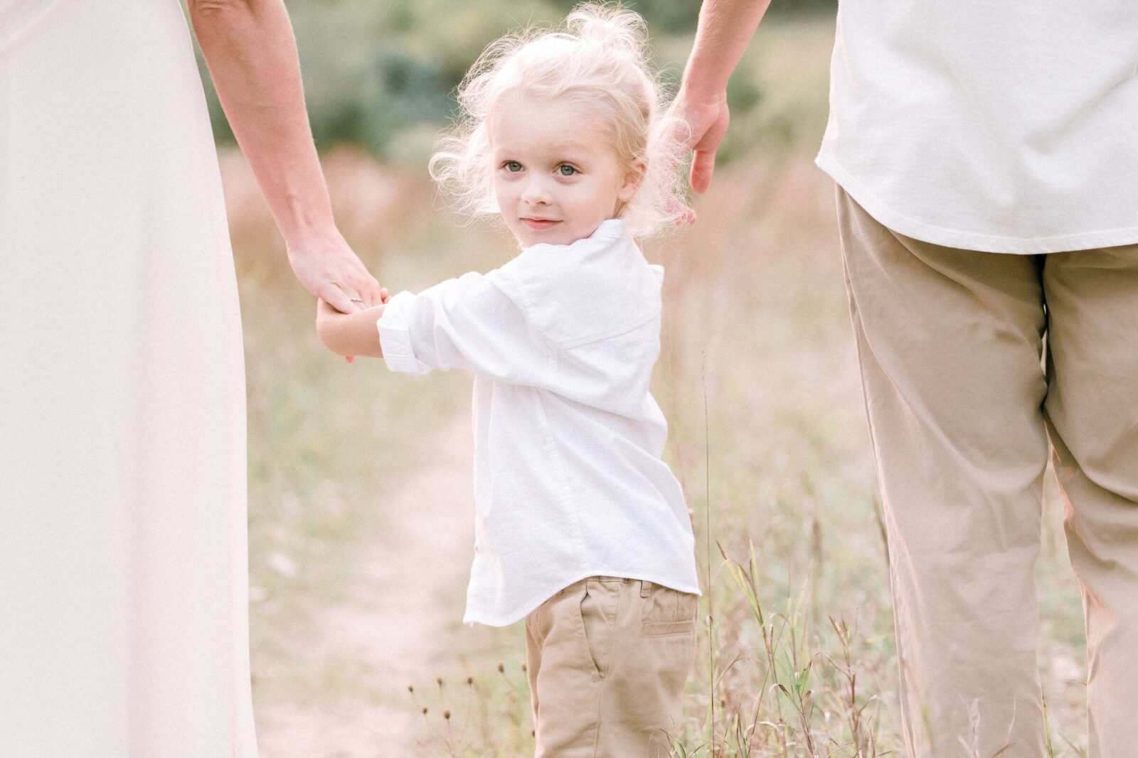 Young child holding both parents' hands during an outdoor family photo session