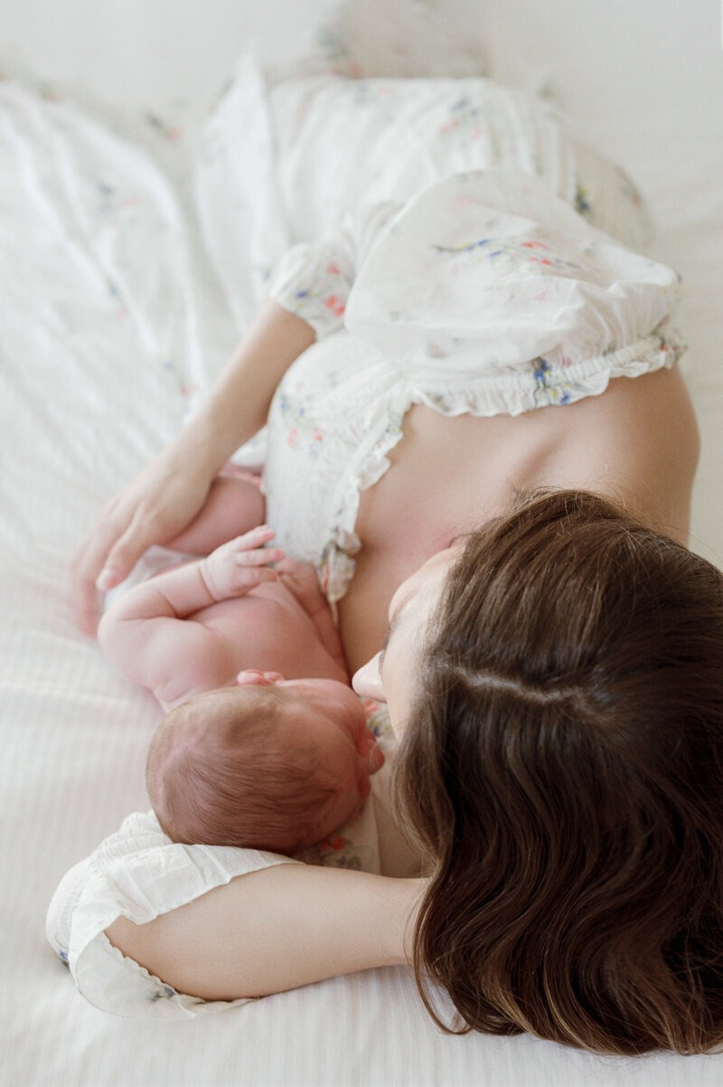 Mother and newborn relaxing together on a bed during an in-home newborn session