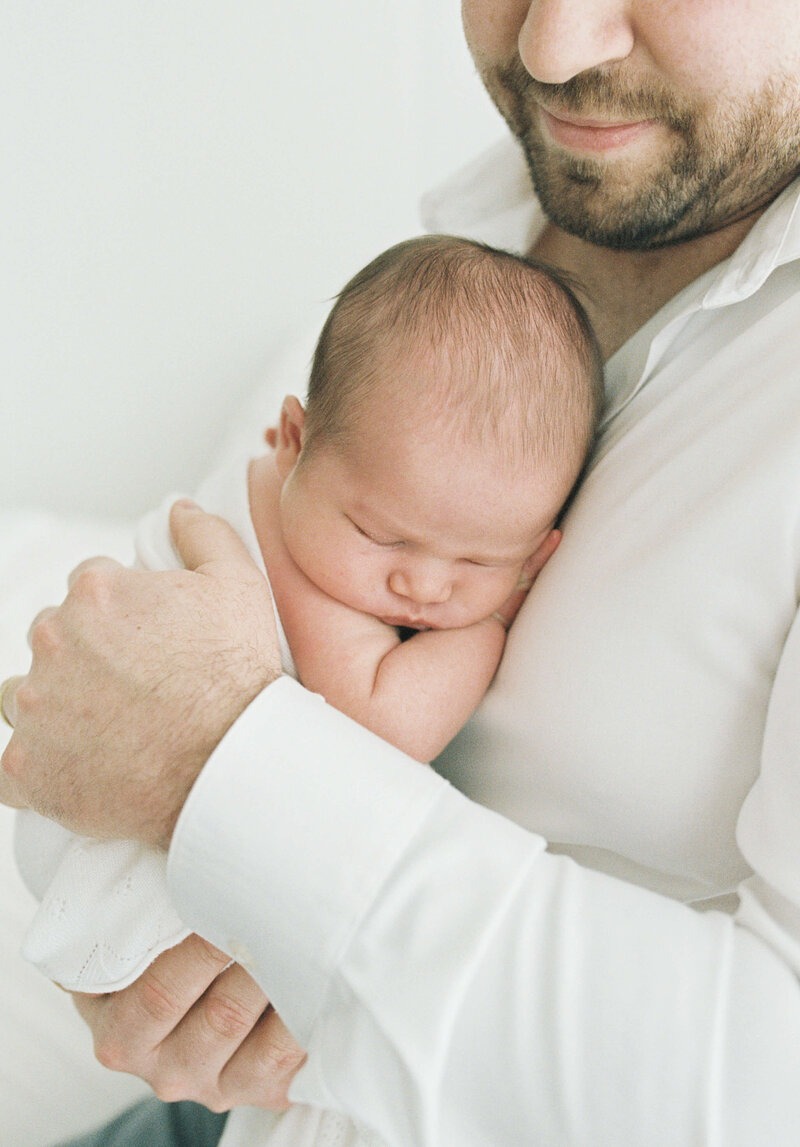 Father holding his sleeping newborn close during a softly lit newborn session