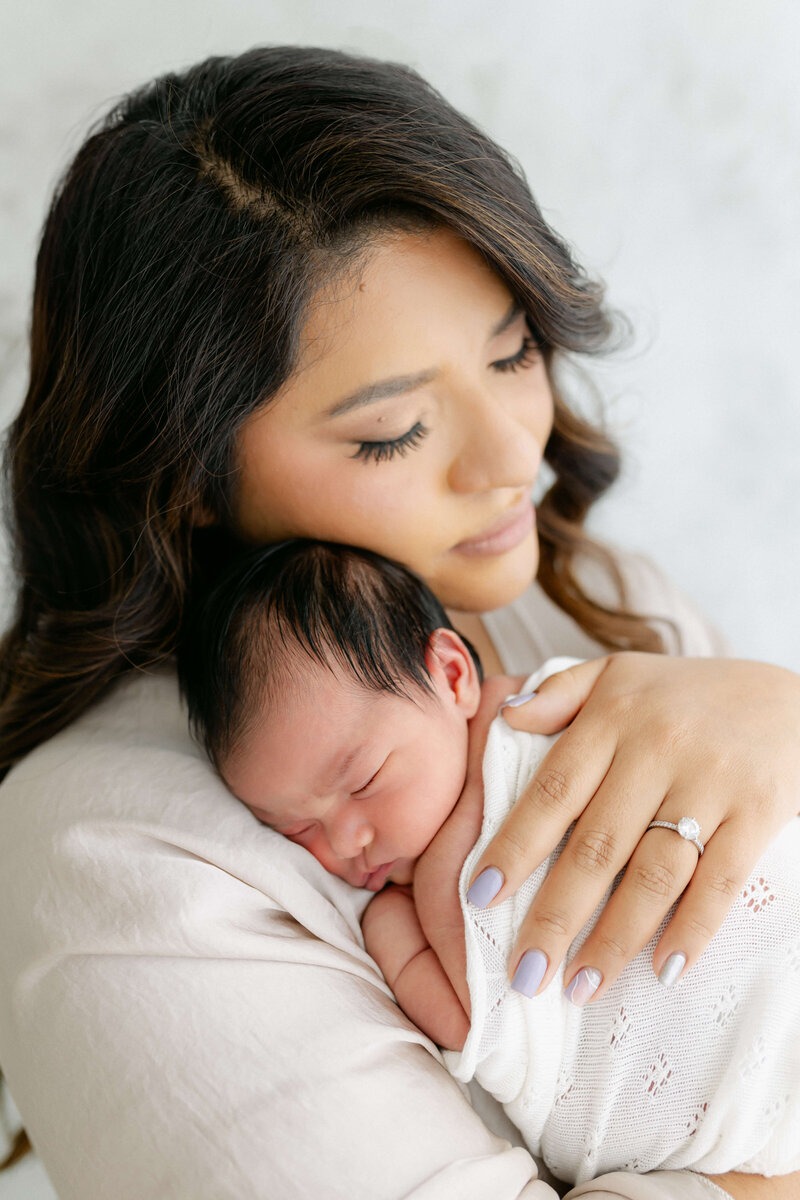 Mother holding her sleeping newborn close during a softly styled newborn portrait session